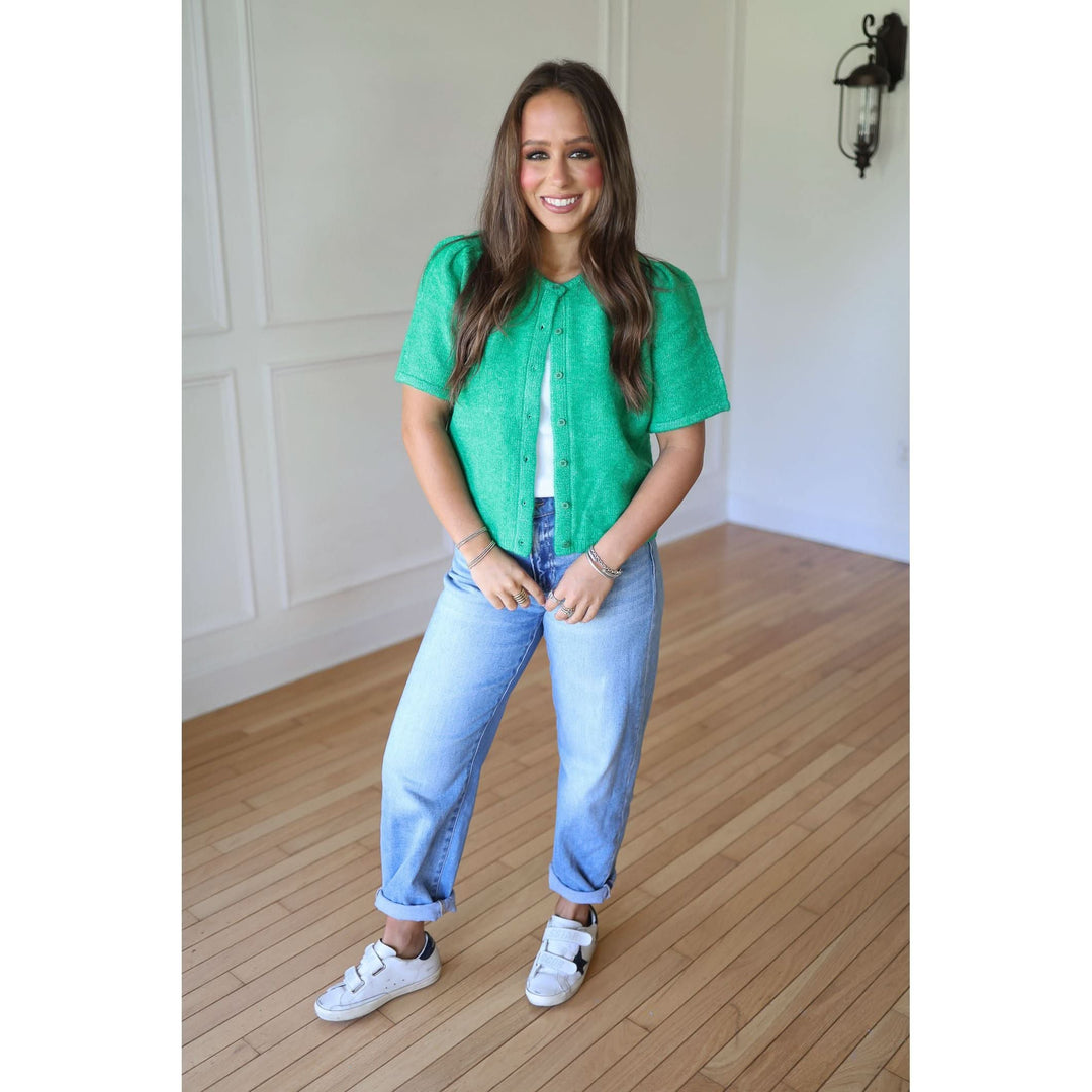 Woman wearing a green blouse, blue jeans, and white sneakers 