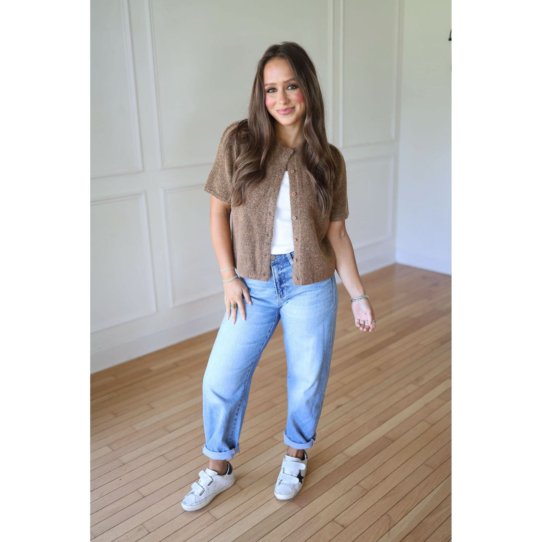 Woman wearing a brown cardigan, white shirt, blue jeans, and white sneakers 
