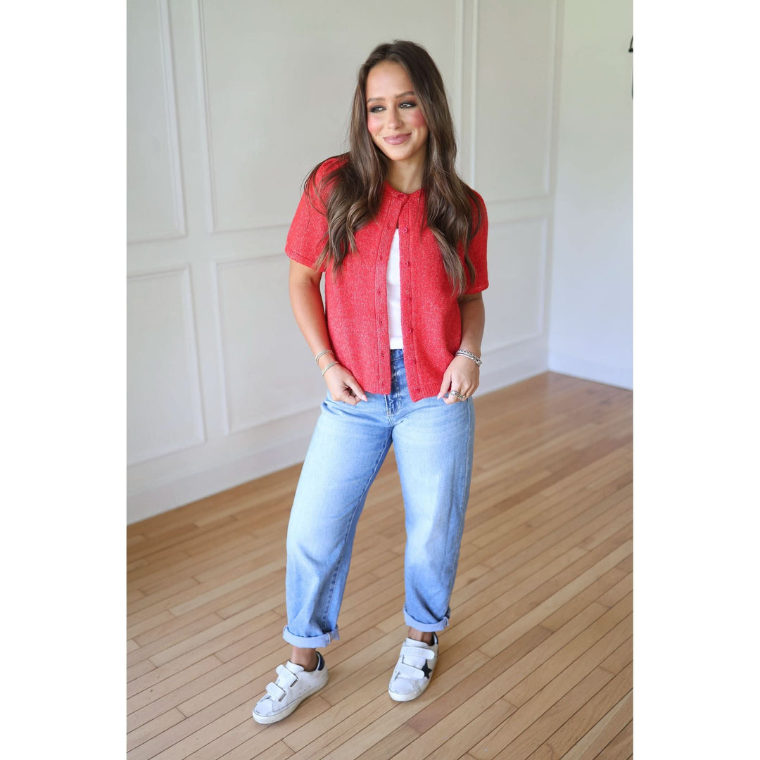 Woman wearing a red shirt, white top, blue jeans, and white sneakers 