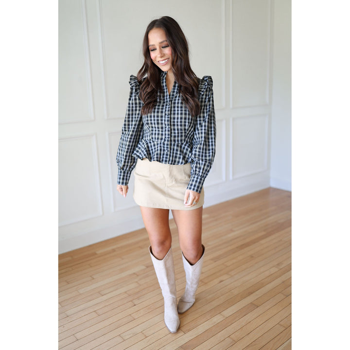 Woman wearing a plaid shirt, beige skirt, and white knee-high boots 
