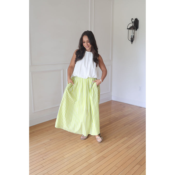 Woman wearing a white top and green striped skirt standing in a room with wooden flooring and white walls.