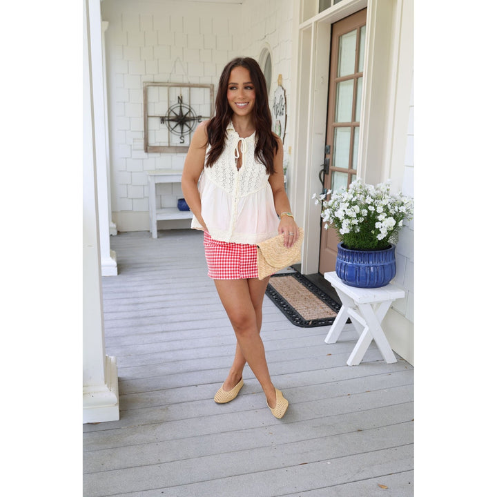 Woman standing on a porch wearing a white blouse and red checkered skirt.