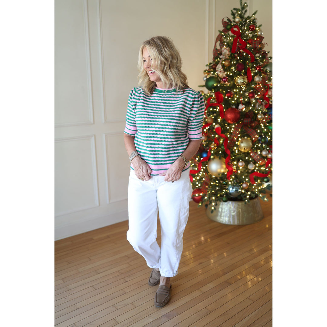 Woman in a striped shirt and white pants standing next to a decorated Christmas tree.