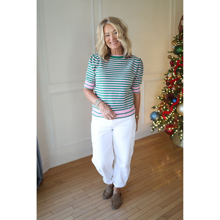 Woman wearing a striped shirt and white pants standing in front of a decorated Christmas tree.