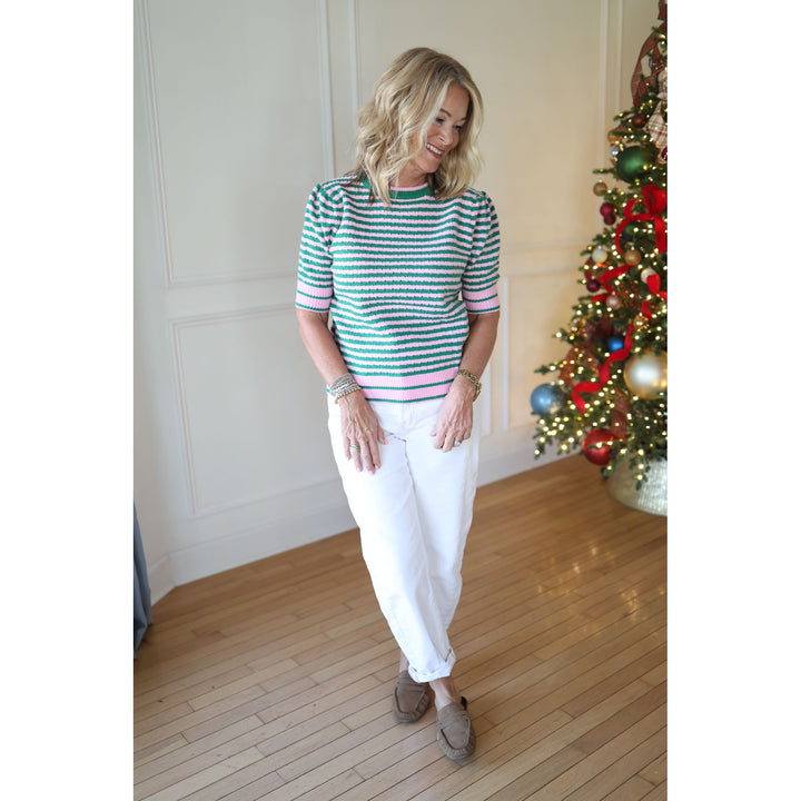 Woman wearing a striped shirt and white pants standing in front of a decorated Christmas tree.