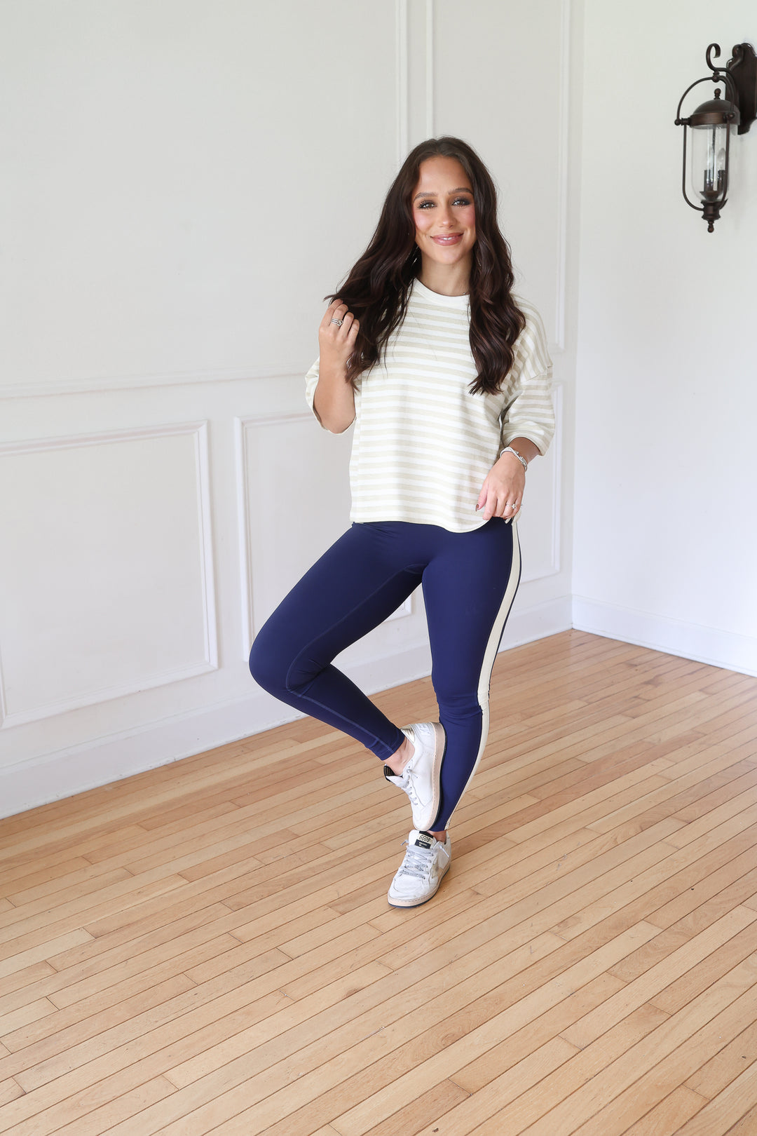 A woman  wearing a cream and white horizontally striped long-sleeve top, navy blue leggings with a white side stripe, and white sneakers.