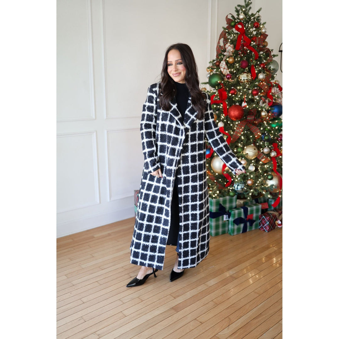 Woman in a checkered coat standing next to a decorated Christmas tree indoors.