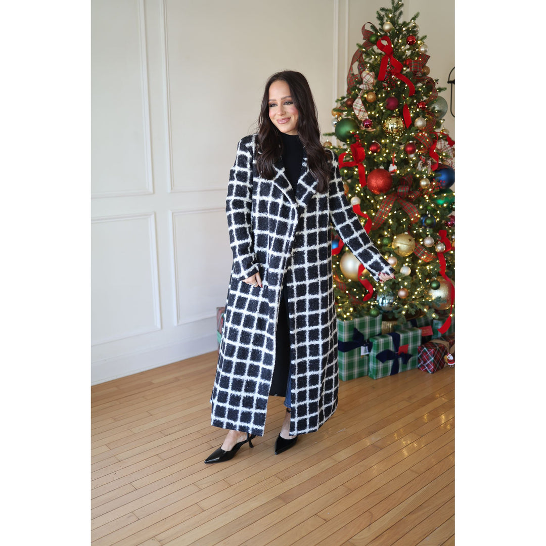 Woman in a checkered coat standing next to a decorated Christmas tree indoors.