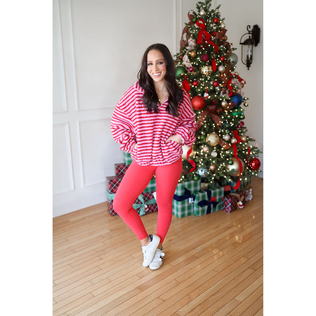 Woman in red and white striped sweater and pink leggings standing in front of a decorated Christmas tree.