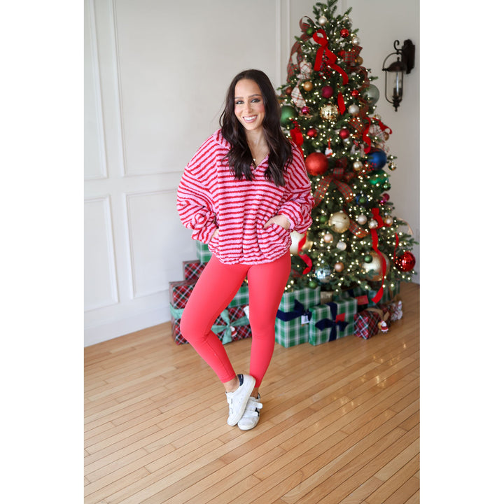 Woman in red and white striped sweater and pink leggings standing in front of a decorated Christmas tree.