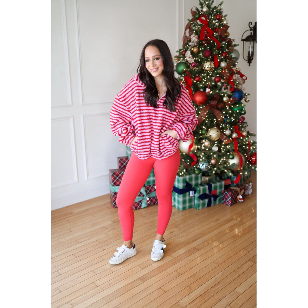 Woman in a red and white striped sweater and pink leggings standing in front of a decorated Christmas tree.
