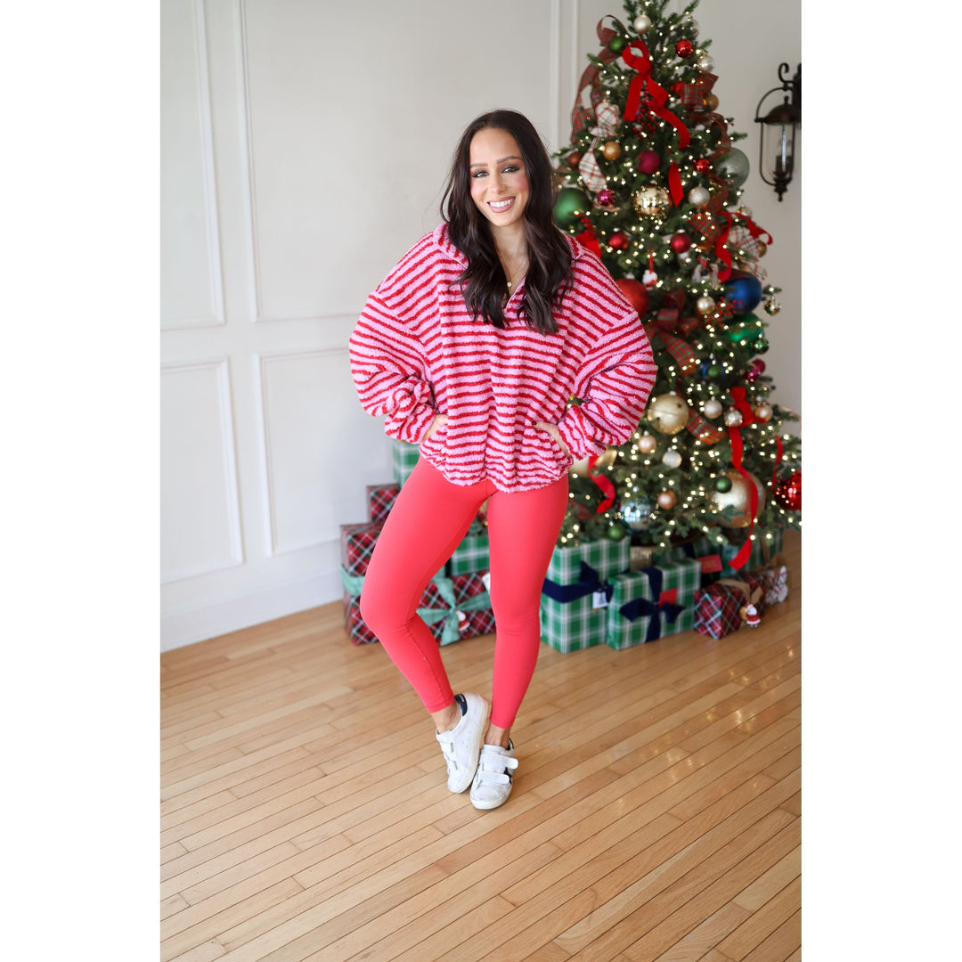 Woman in red and white striped sweater and pink leggings standing in front of a decorated Christmas tree.