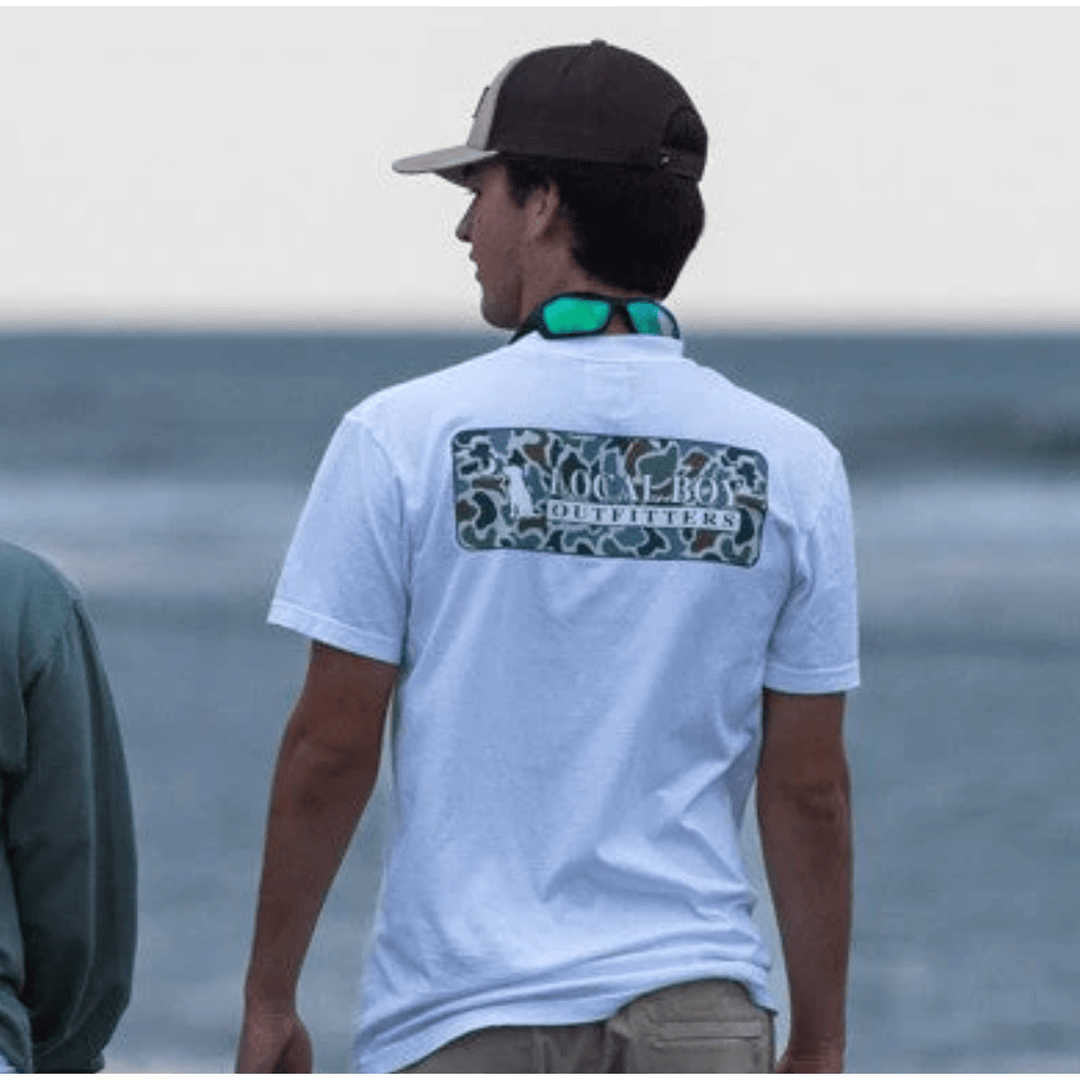 Man wearing a white t-shirt with a logo on the back, standing by the water.