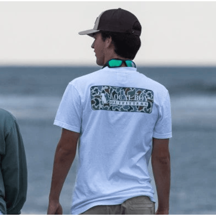 Man wearing a white t-shirt with a logo on the back, standing by the water.