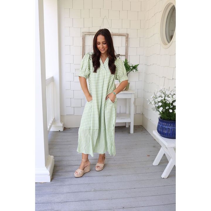 Woman in a green checkered dress standing on a wooden deck with white walls and decor.