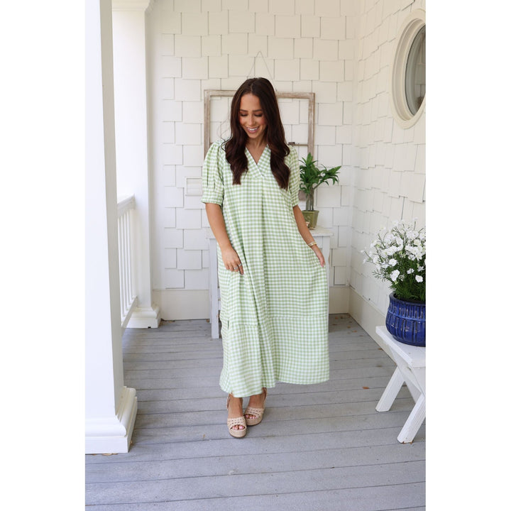 Woman wearing a green checkered dress on a wooden porch.