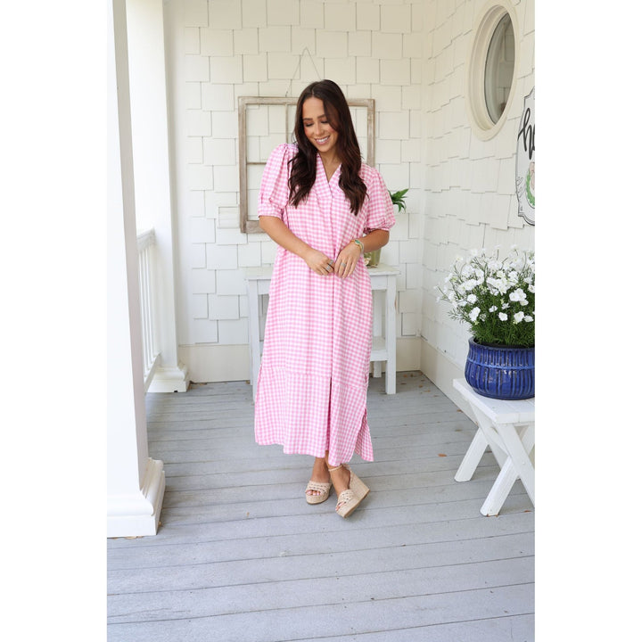 Woman in a pink checkered dress standing on a wooden deck with white walls and decor.