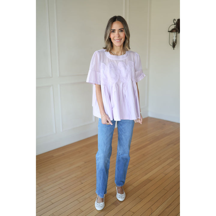 Woman wearing a light purple top and blue jeans indoors.
