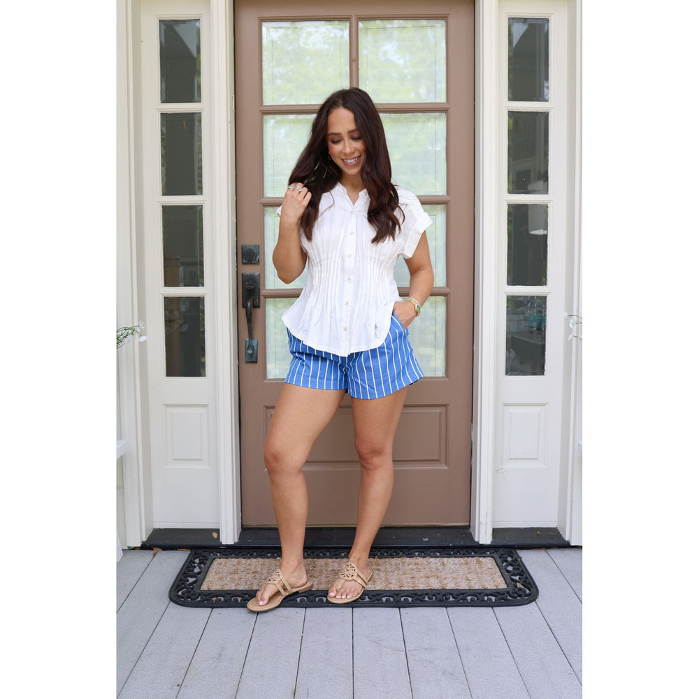 Woman in a white blouse and blue shorts standing in front of a door.
