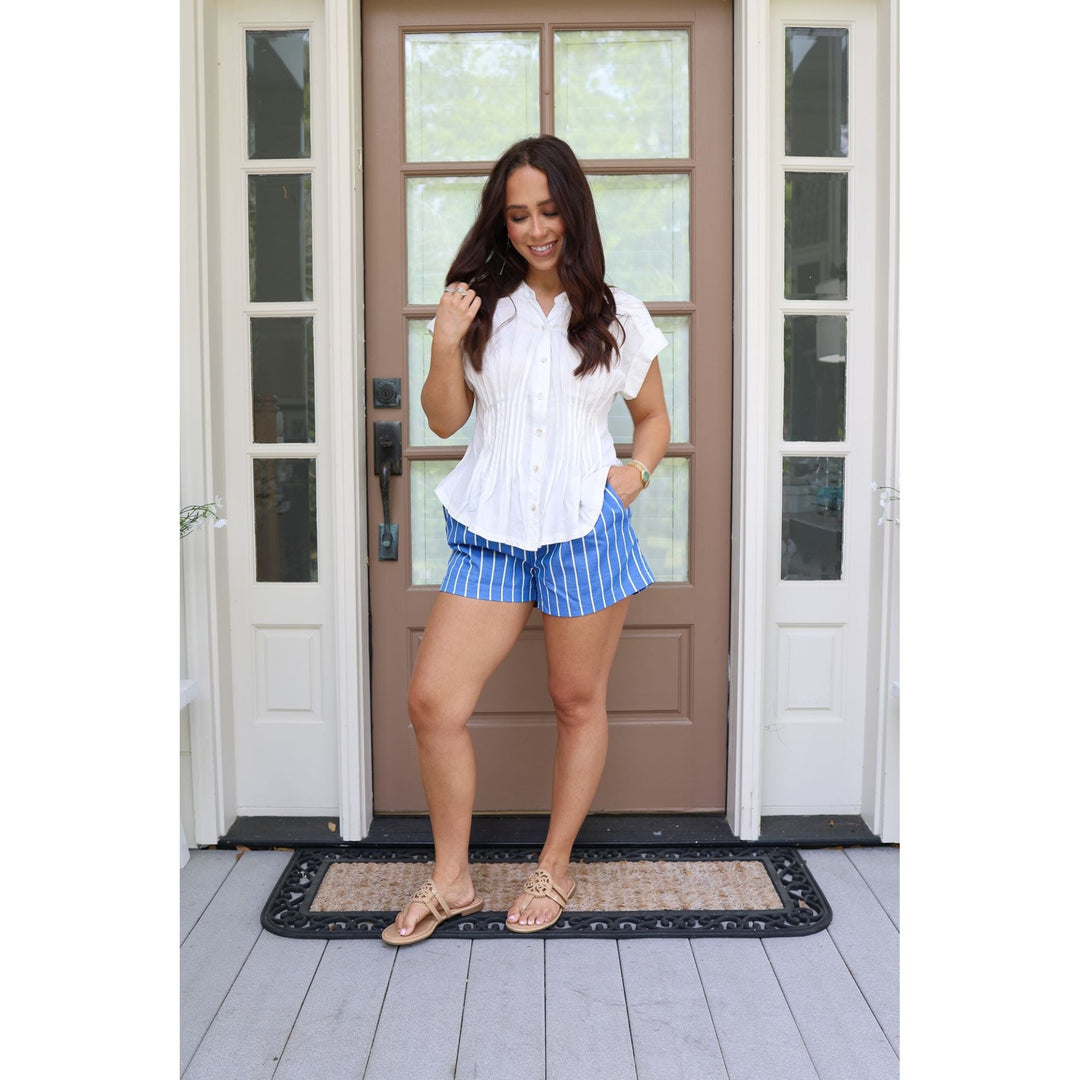 Woman in a white blouse and blue shorts standing in front of a door.