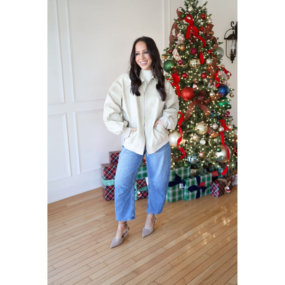 Woman in a cream jacket and blue jeans standing in front of a decorated Christmas tree.