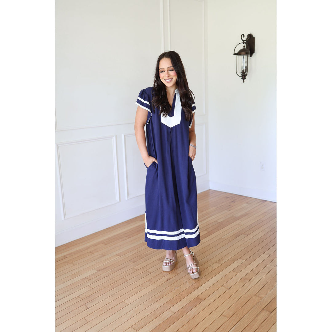 Woman wearing a blue dress with white accents in a room with wooden flooring and white walls.