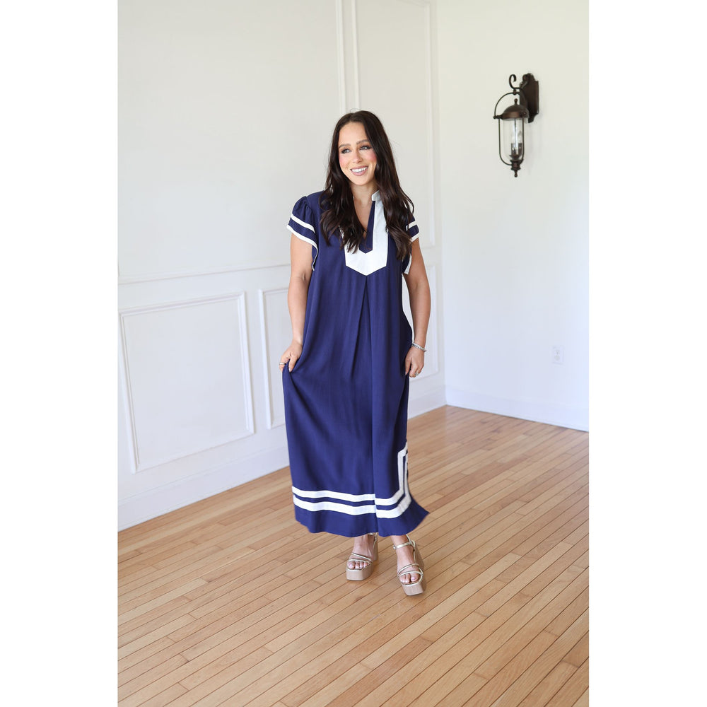 Woman wearing a blue dress with white accents in a room with wooden flooring and white walls.