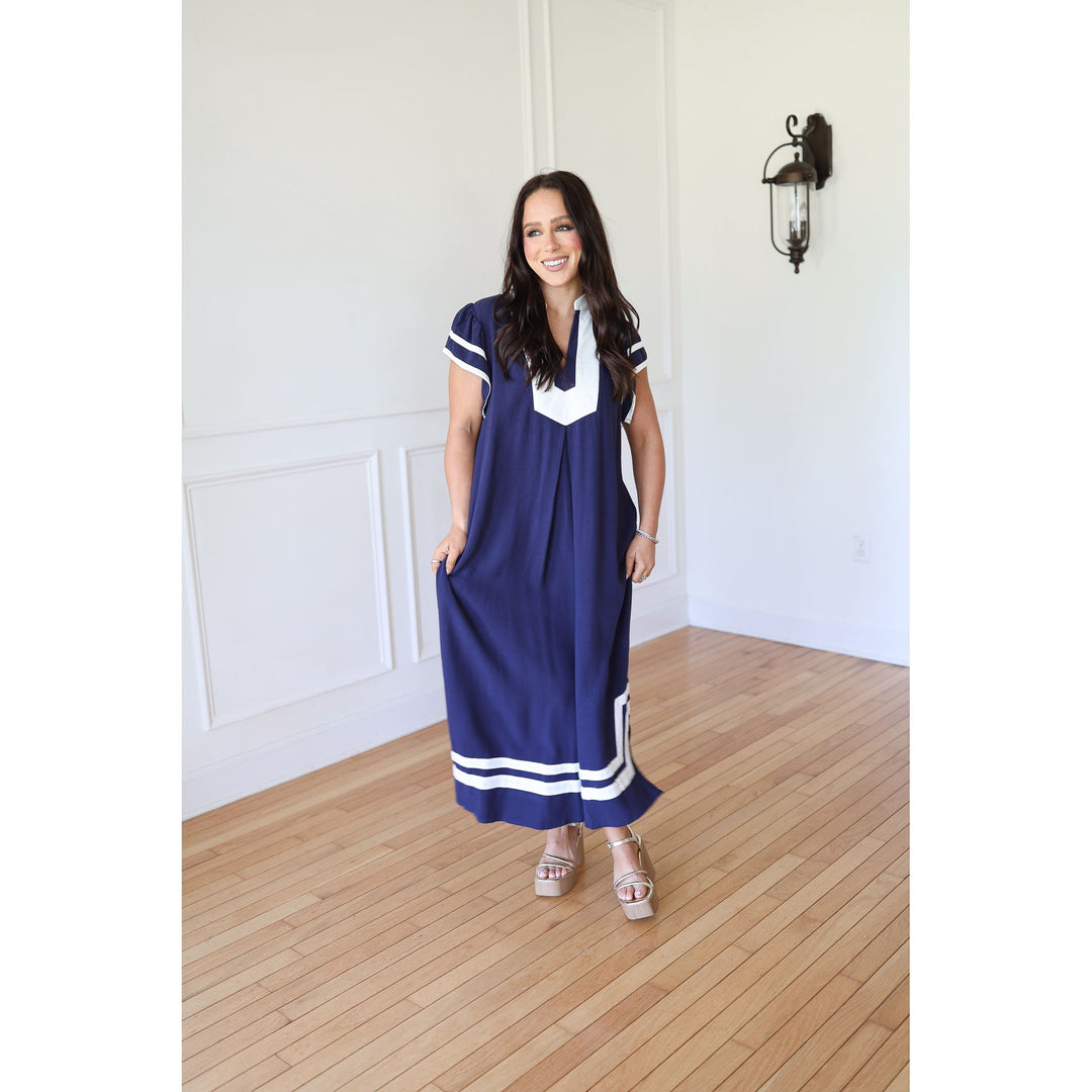 Woman wearing a blue dress with white accents in a room with wooden flooring and white walls.