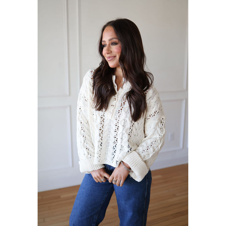 Woman wearing a cream knitted sweater and blue jeans indoors.