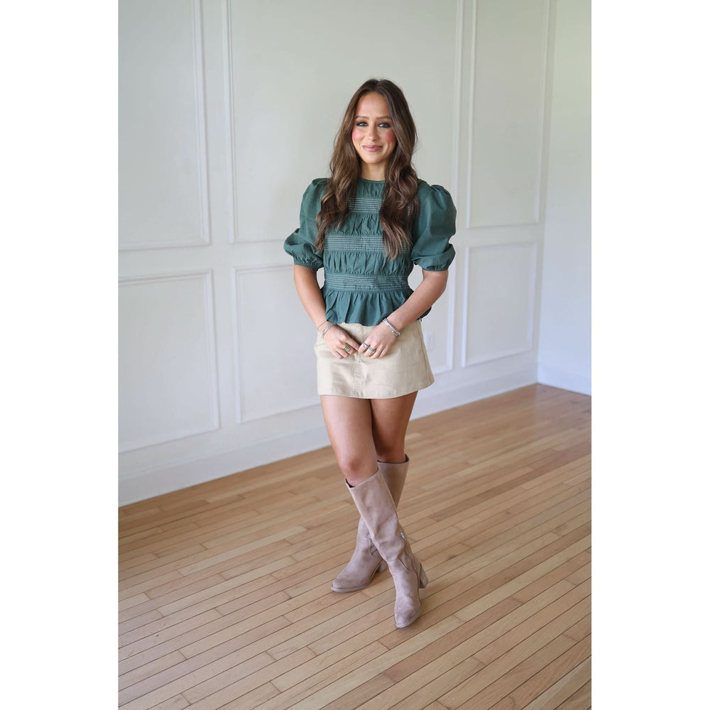 Woman wearing a green top and beige skirt with knee-high boots 
