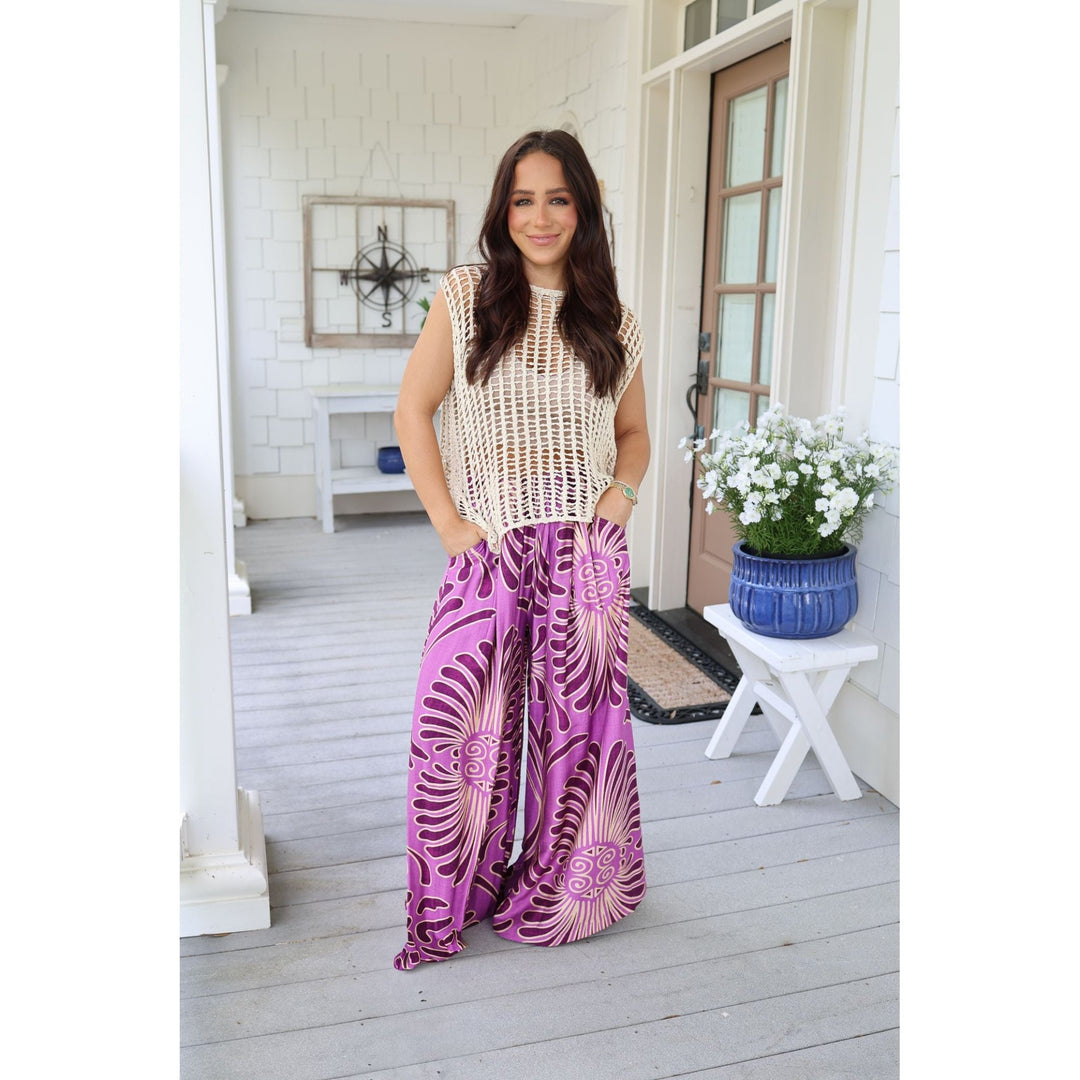 Woman in a white sleeveless top and purple patterned pants standing on a porch.