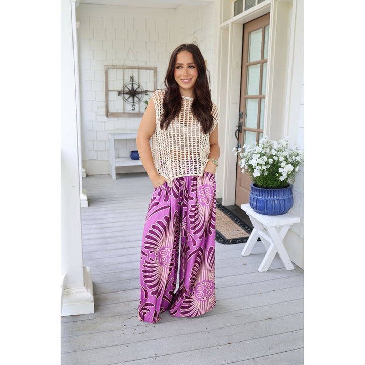 Woman wearing a sleeveless crochet top and purple patterned pants on a porch.