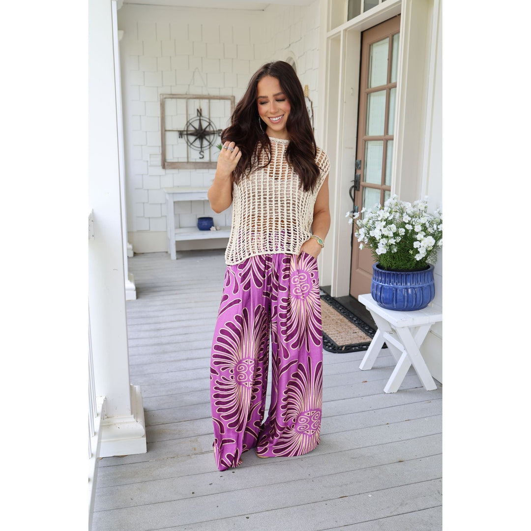 Woman in a beige top and purple patterned pants standing on a porch.