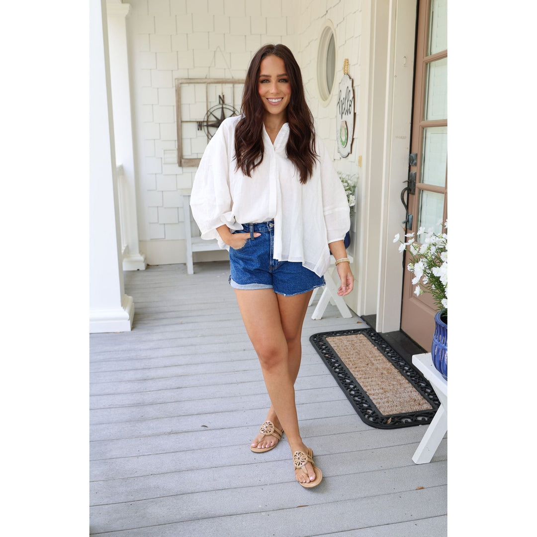 Woman in white blouse and blue shorts standing on a porch.