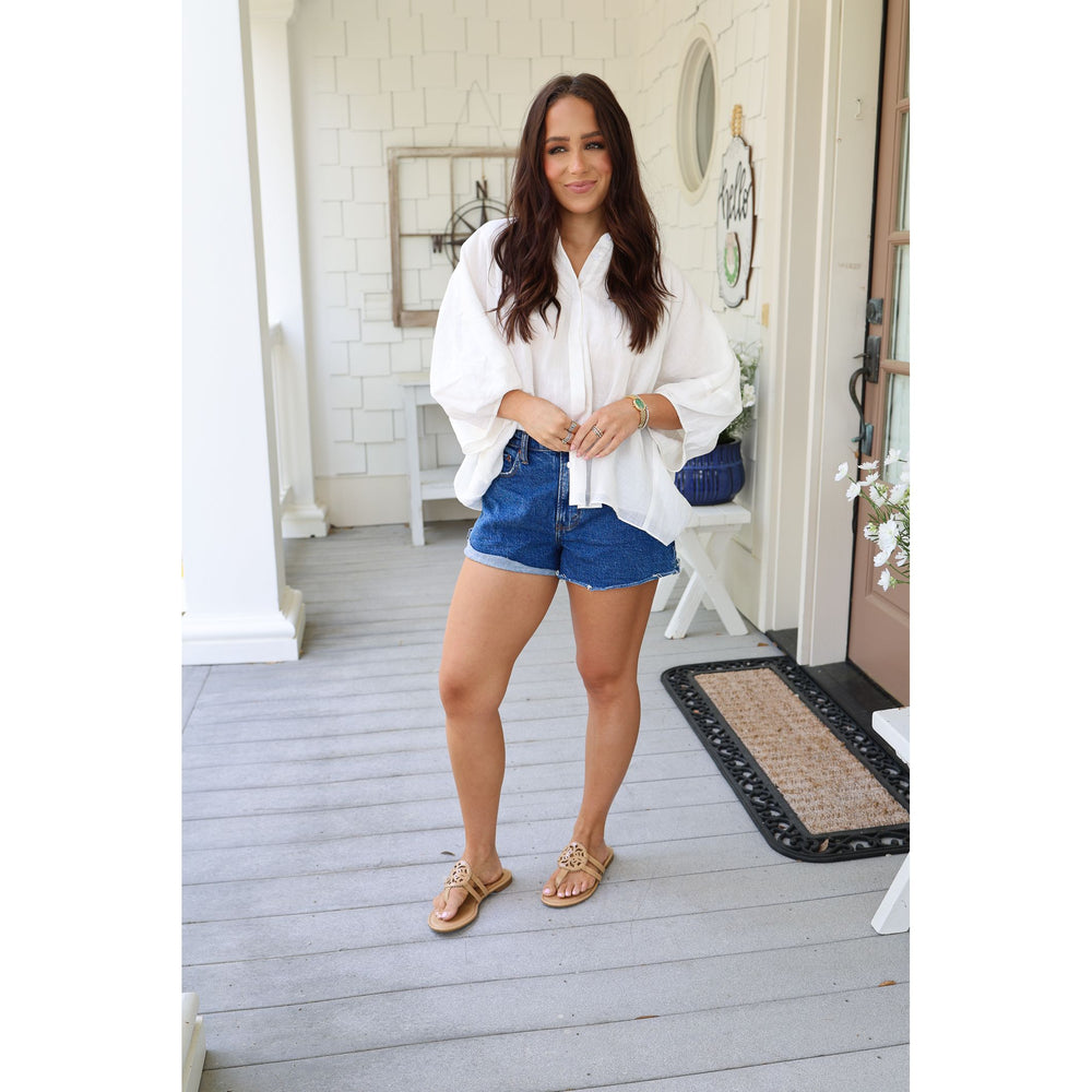 Woman standing on a porch wearing a white shirt and blue shorts.