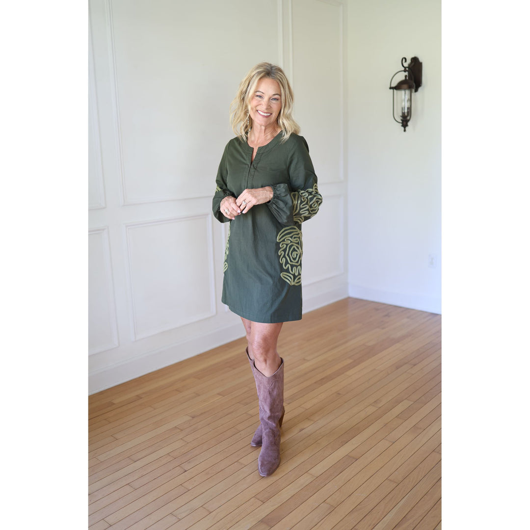 Woman wearing a green dress with patterned sleeves and brown boots 