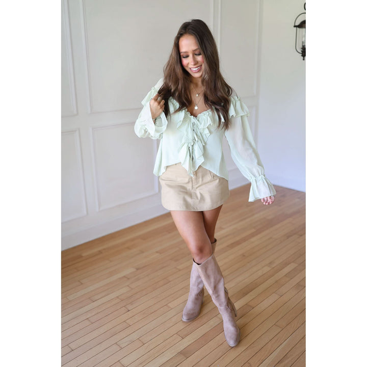 Woman wearing a light green blouse, beige shorts, and beige knee-high boots 