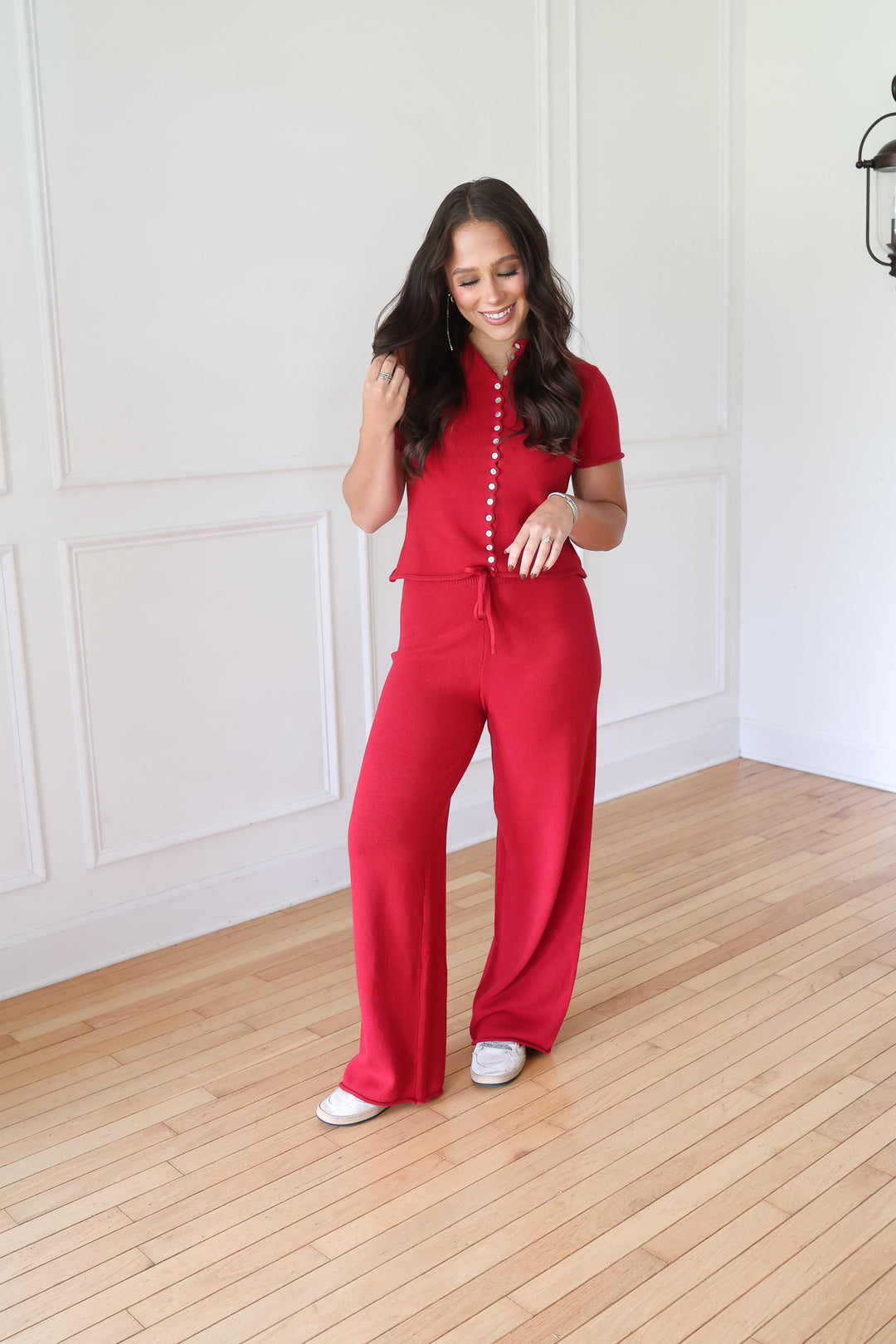 A woman modeling a bright red short-sleeve jumpsuit with a buttoned collar and drawstring waist