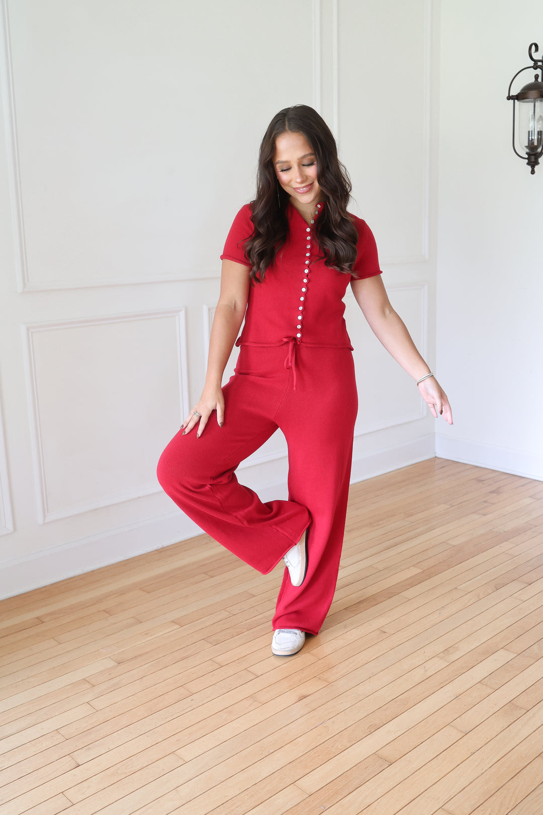 A woman modeling a bright red short-sleeve jumpsuit with a drawstring waist and decorative front buttons