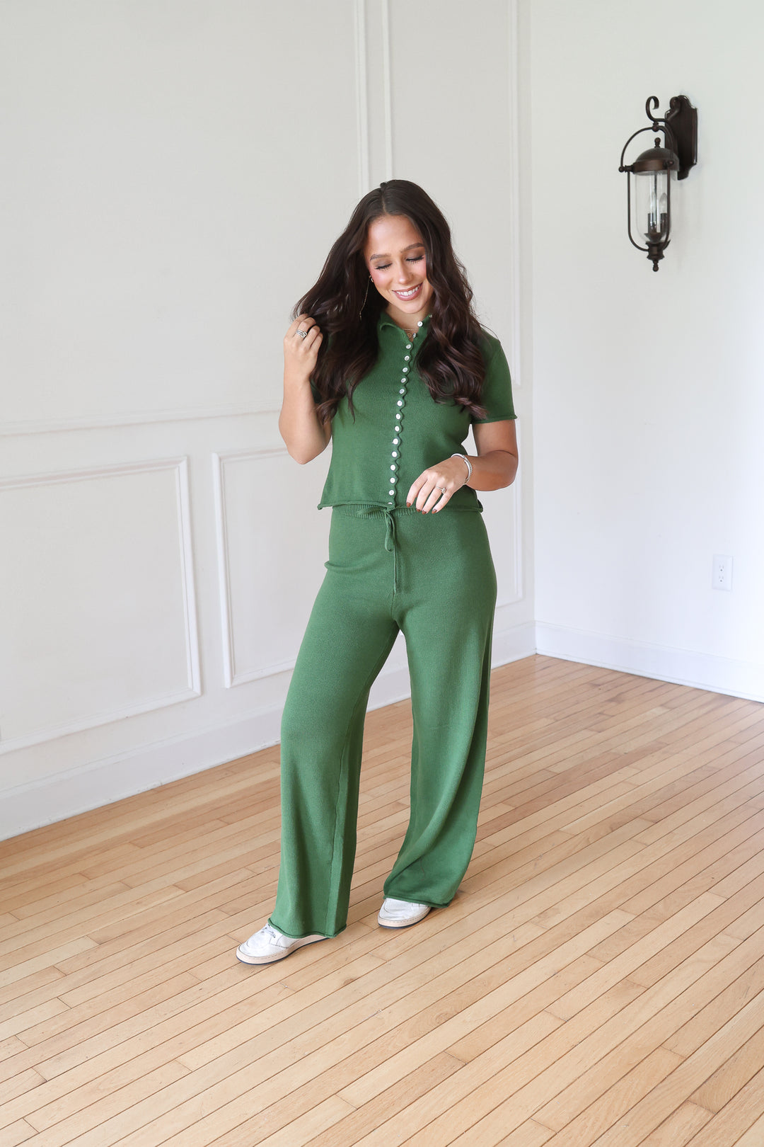 A woman modeling a matching green two-piece set consisting of a short-sleeve button-front top and wide-leg pants.