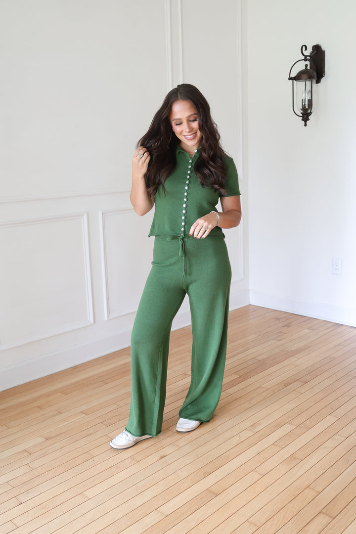 A woman modeling a matching green two-piece set consisting of a short-sleeve button-front top and wide-leg pants.
