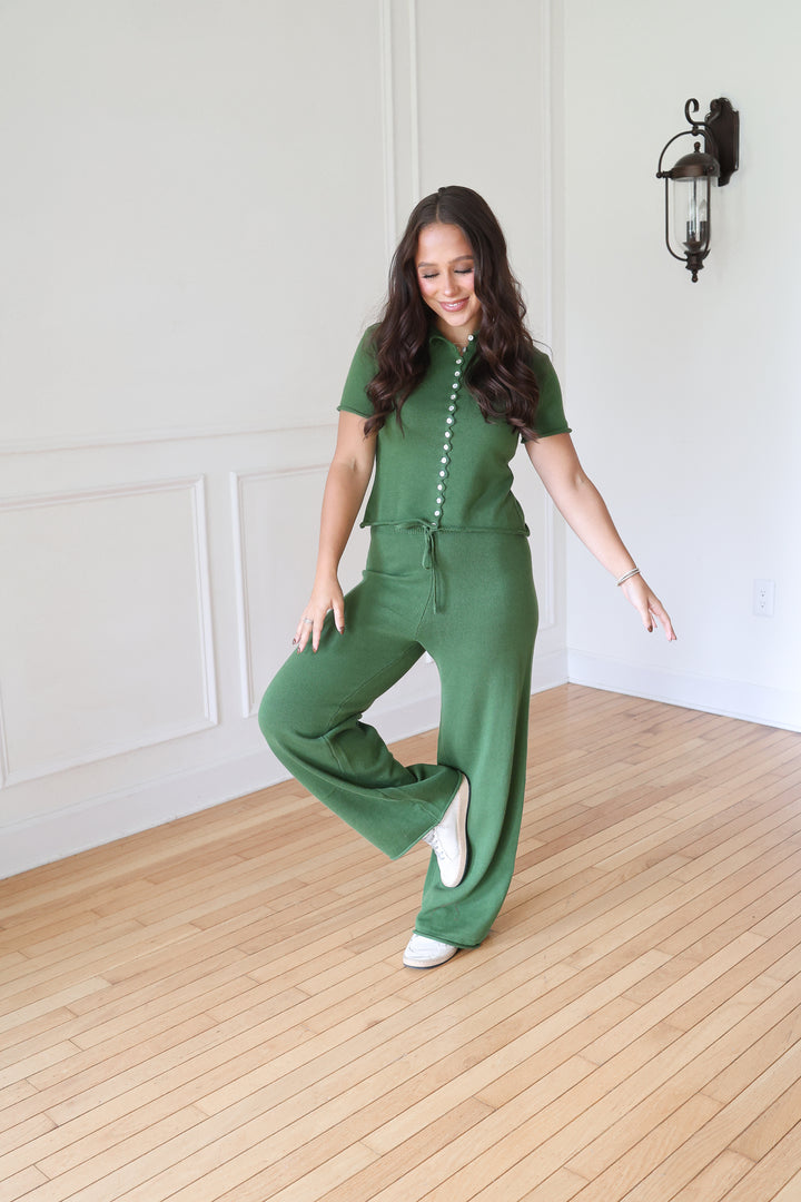 A woman modeling a green short-sleeve jumpsuit with a buttoned front and drawstring waist