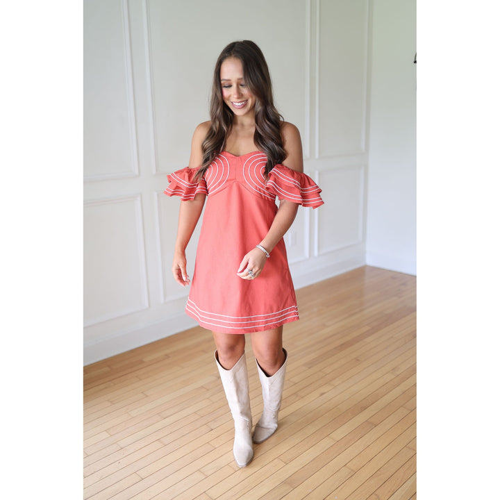 Woman wearing a coral dress with white trim and white boots 