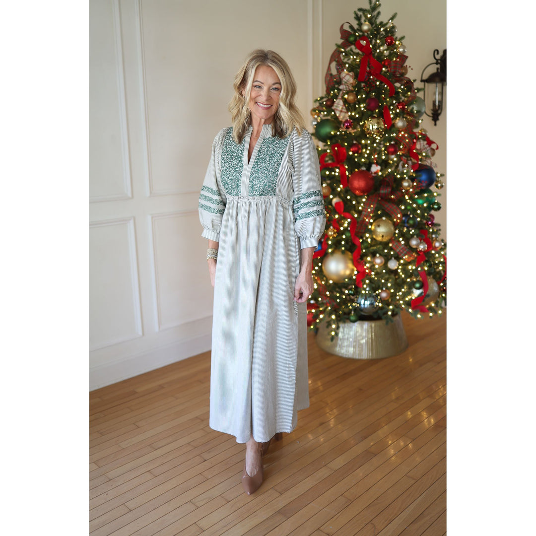 Woman in a green striped  dress standing next to a decorated Christmas tree indoors.