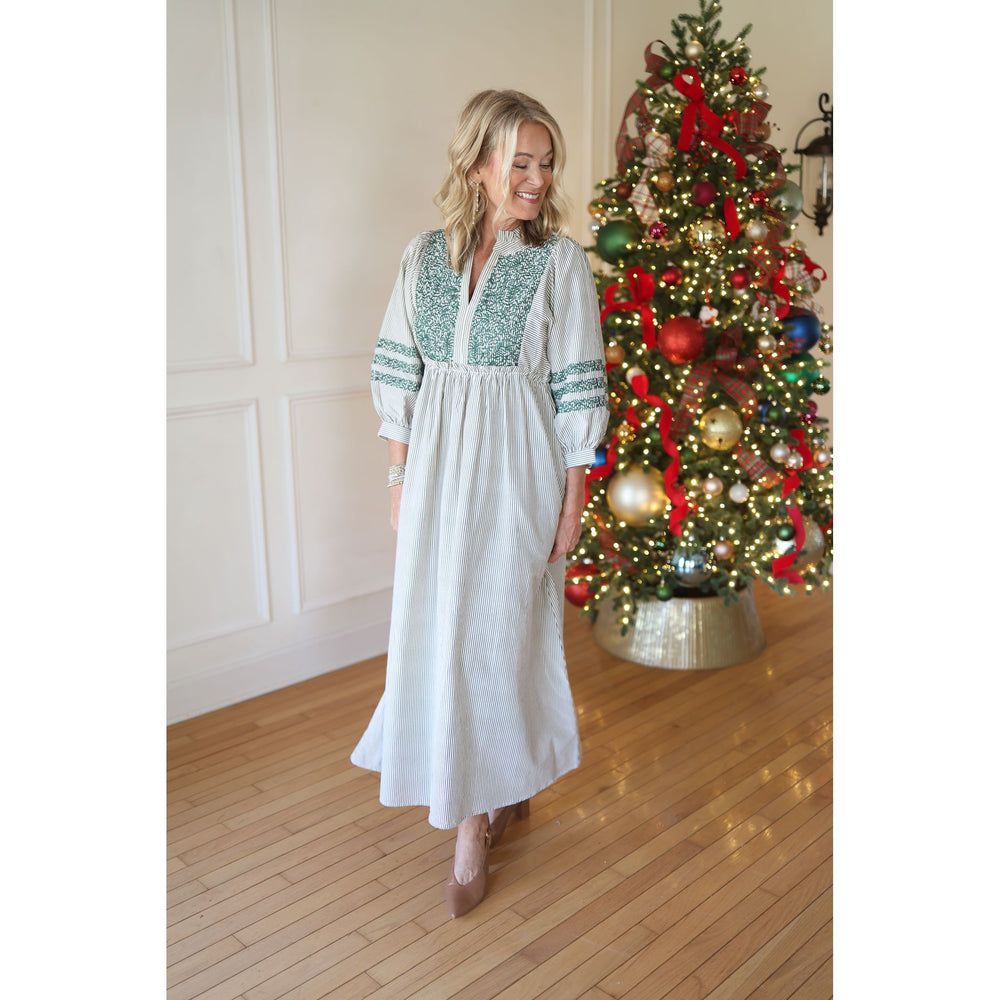Woman in a white striped dress with green embroidery standing in front of a decorated Christmas tree.