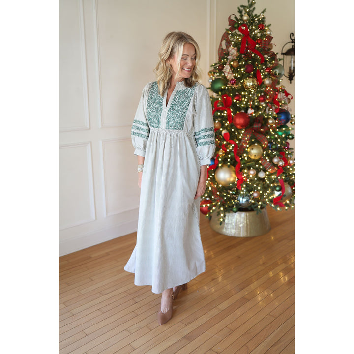 Woman in a white striped dress with green embroidery standing in front of a decorated Christmas tree.