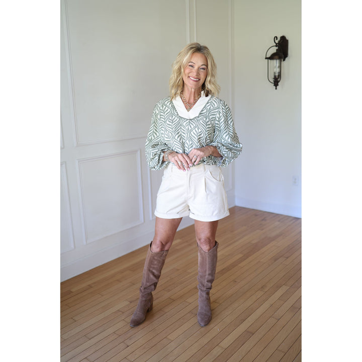 Woman wearing a patterned sweater, white shorts, and brown knee-high boots 