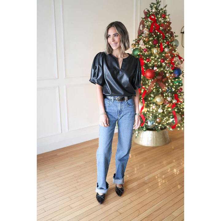 Woman in black top and blue jeans standing in front of a decorated Christmas tree.