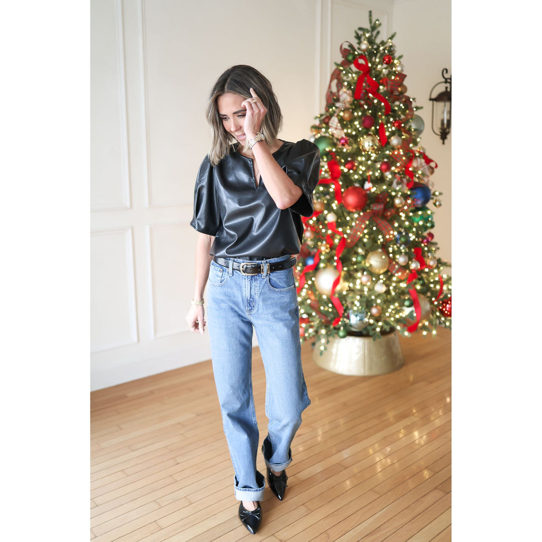 Woman in black top and blue jeans standing in front of a decorated Christmas tree.