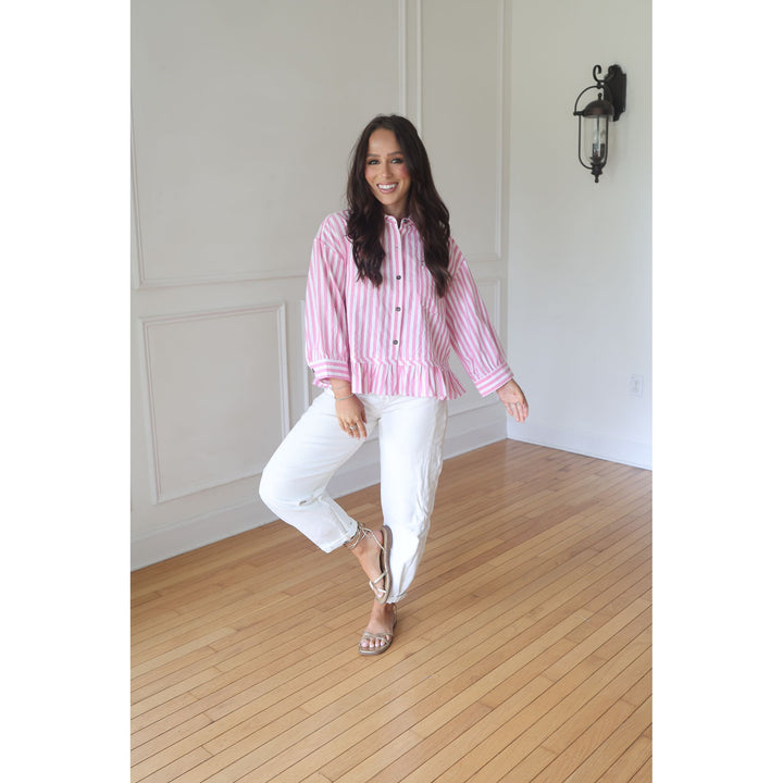 Woman in a pink striped shirt and white pants standing on a wooden floor.